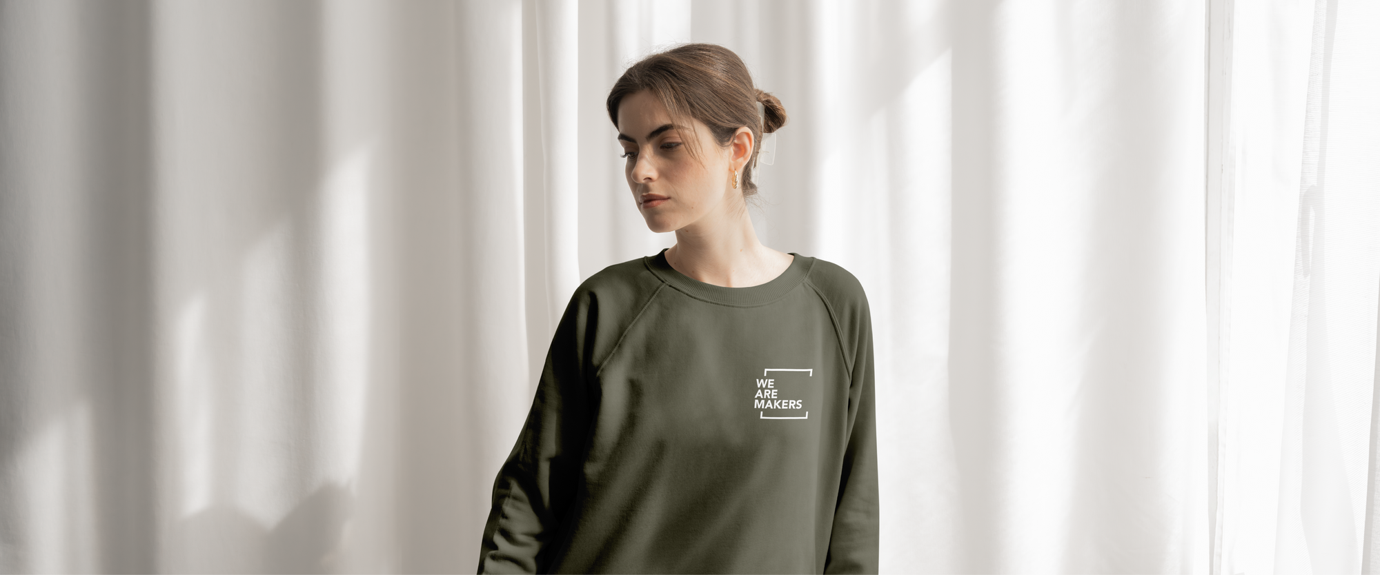 Person wearing a green sweatshirt with a logo against a white curtain background